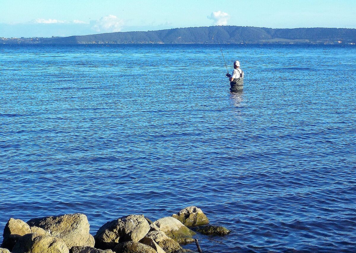 A fisherman casting a rod on a calm lake